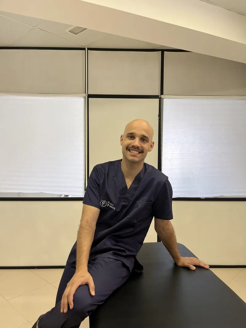 Eduard Folch, fisioterapeuta y osteópata, sonriente y sentado en una camilla de la consulta